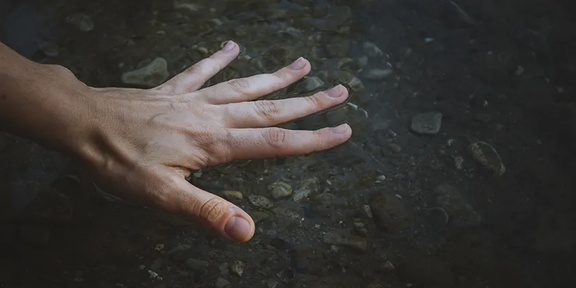 Hand berührt ruhiges Gewässer: Moment der Energetik und Traumaheilung.